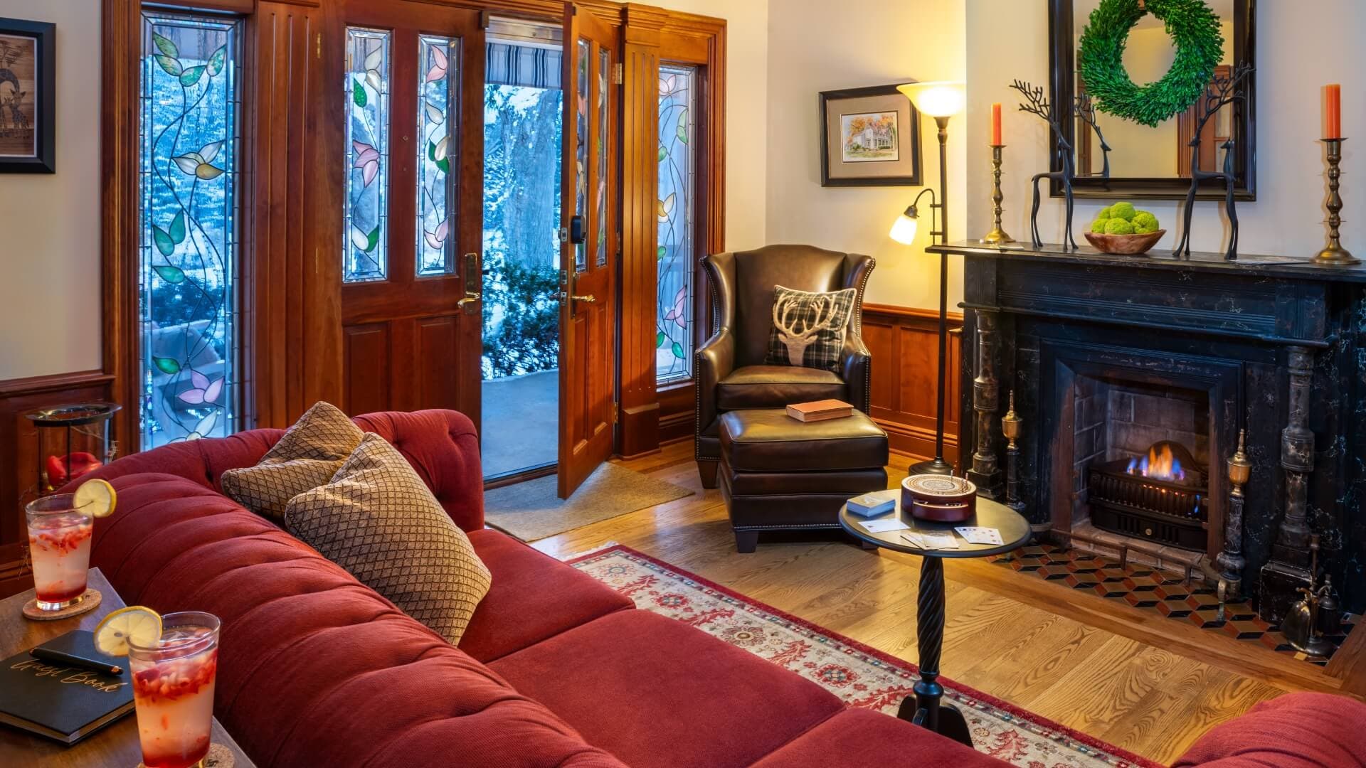 A cozy living room with a red sofa, fireplace, and welcoming wooden doors.